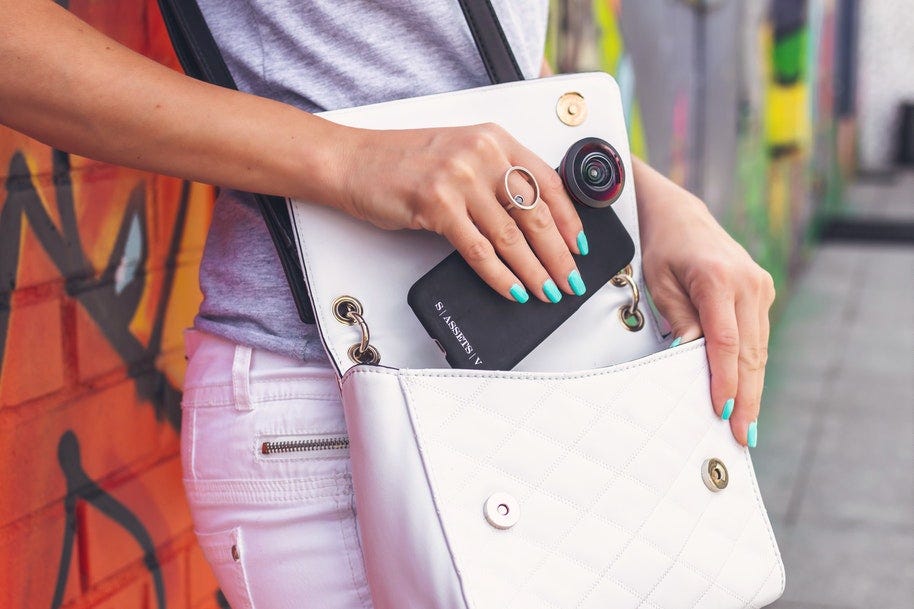 woman putting smartphone with camera lens in bag