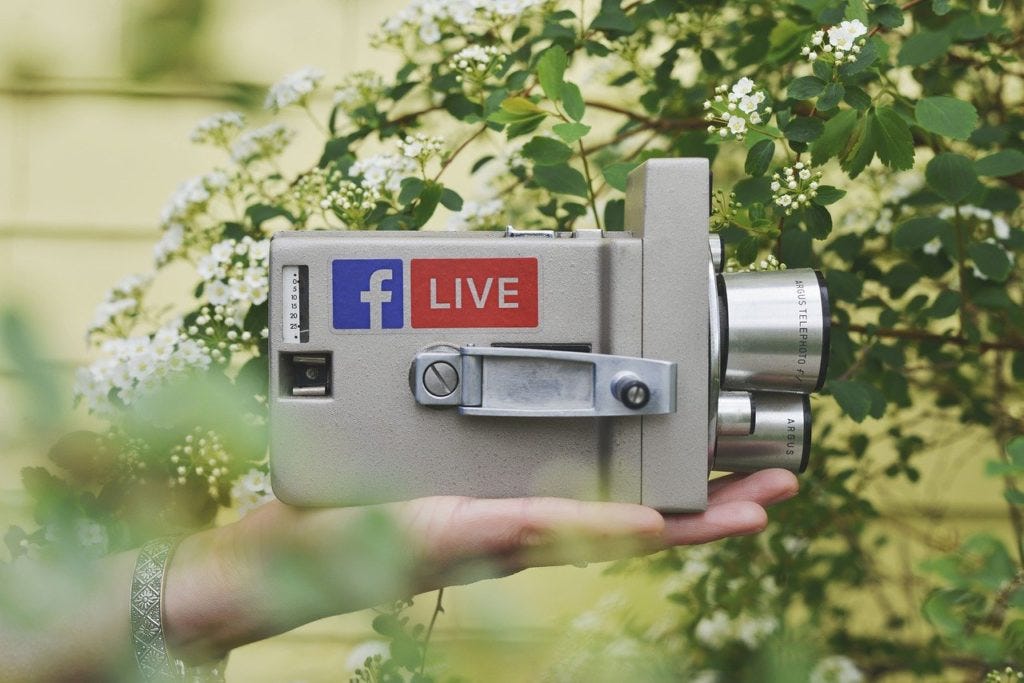 A person holding a vintage camera that has a sticker of Facebook Live on it.